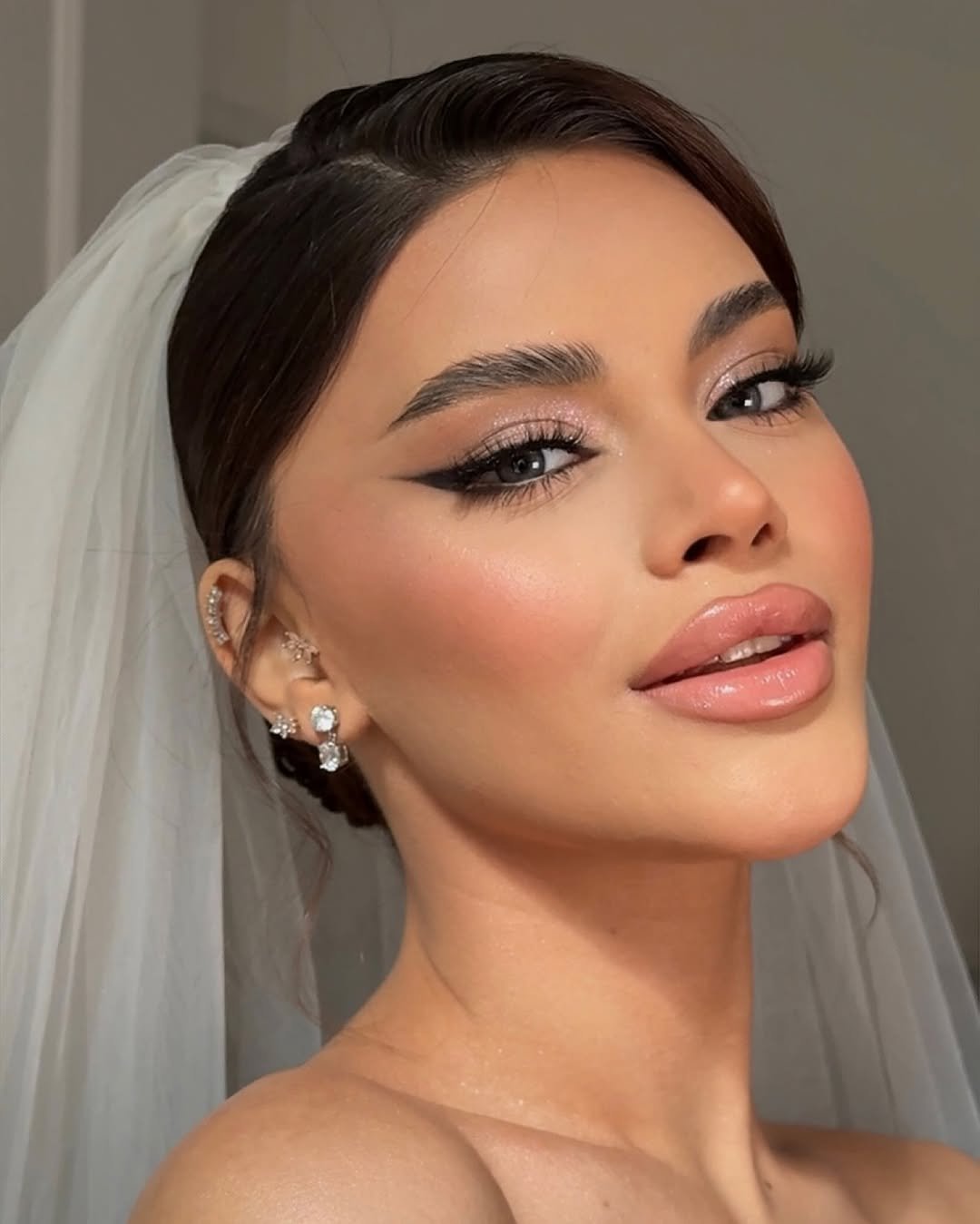 Arab bridal makeup in Dubai with sharp winged liner, glowing skin, glossy nude lips and a white veil