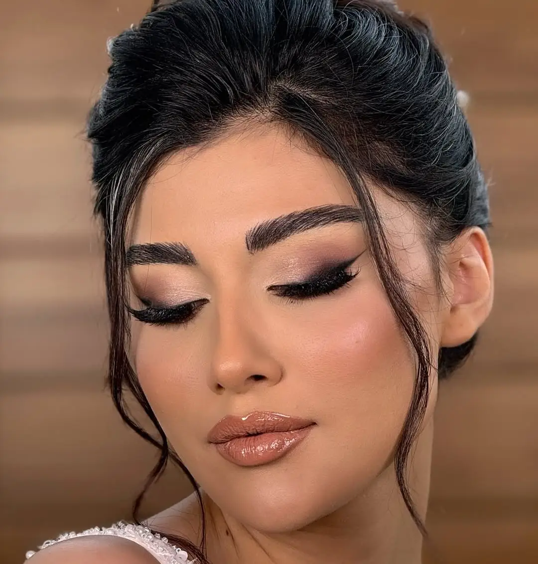 Close-up bridal smokey eye look with winged liner, full lashes, glowing skin and glossy nude lips